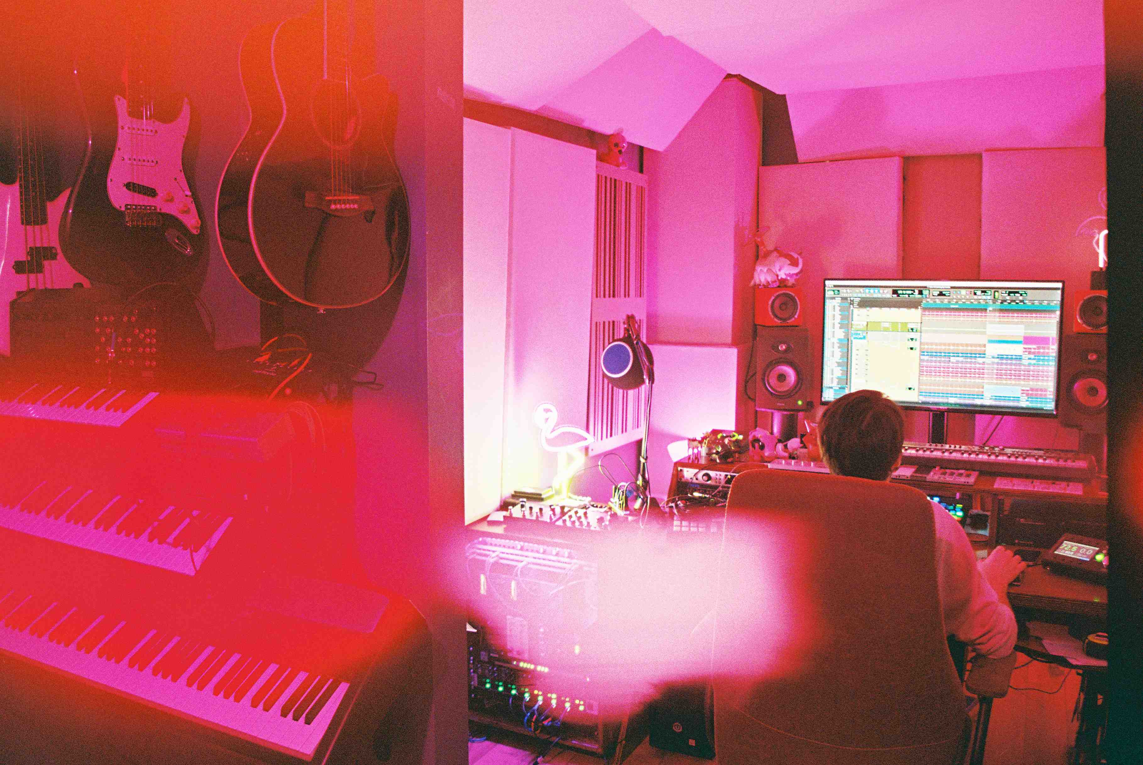 Synthesizers and guitars hanging on a wall with Robby working in the background