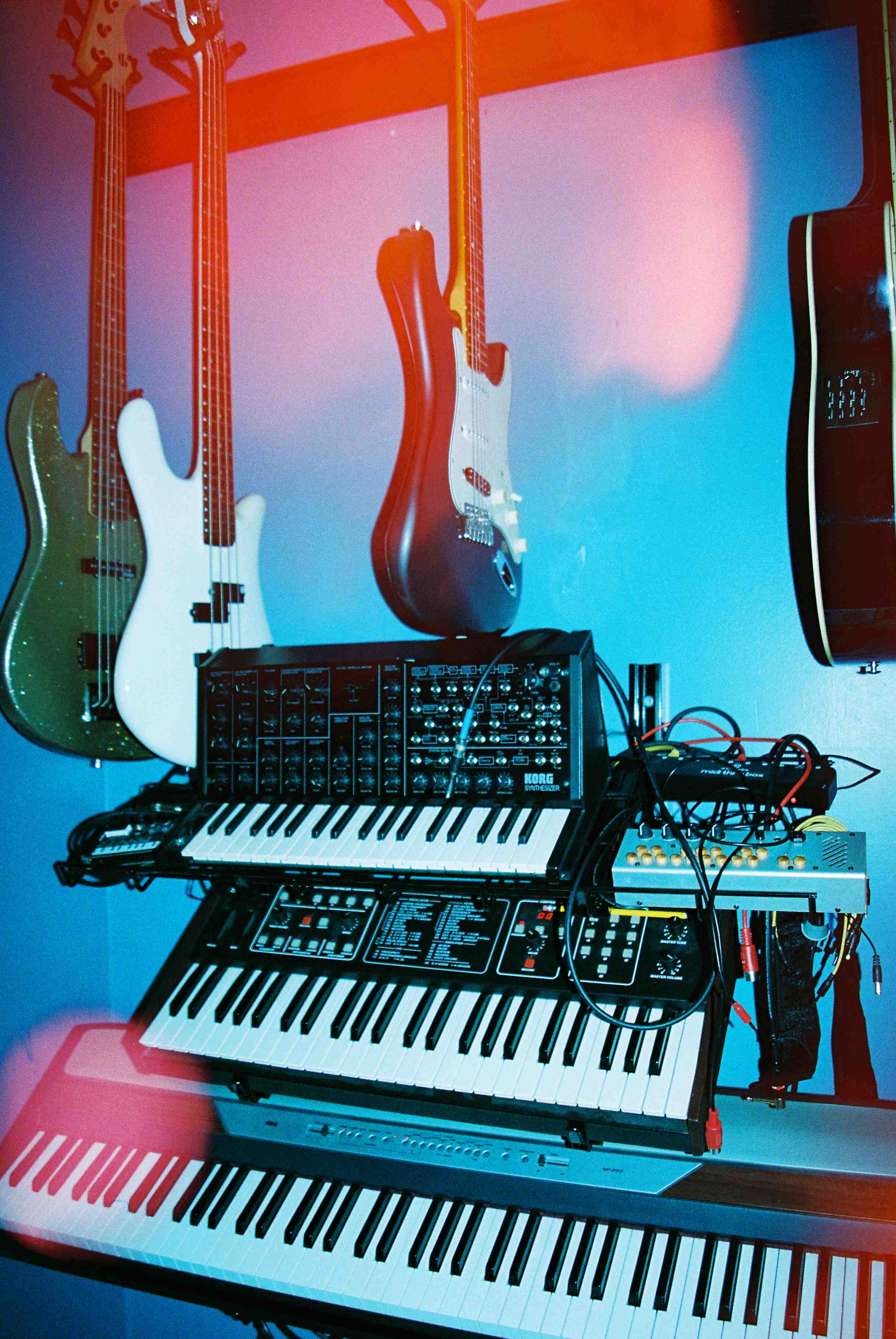 Synthesizers and guitars hanging on a wall with other tools to produce music