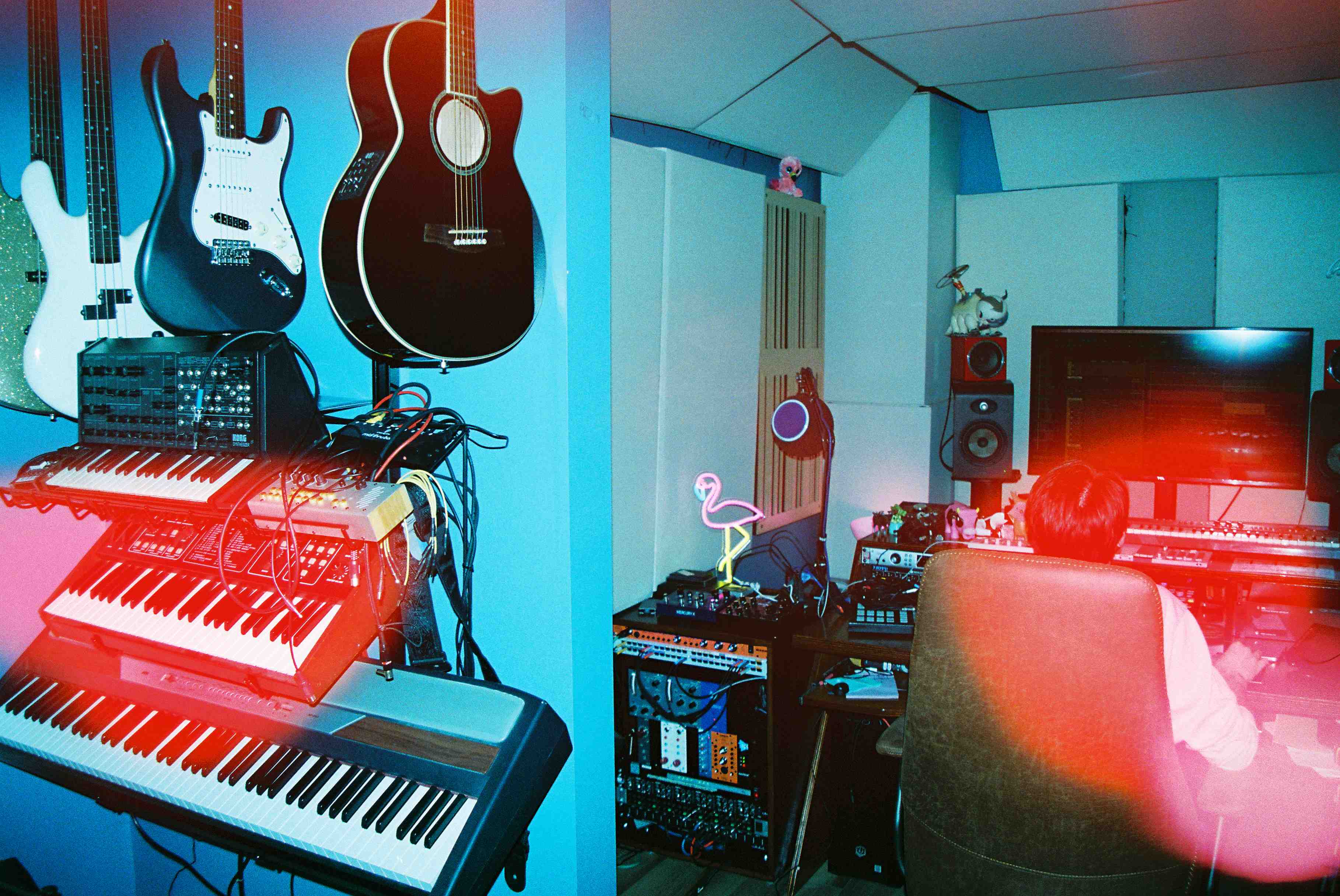 Synthesizers and guitars hanging on a wall with Robby working in the background